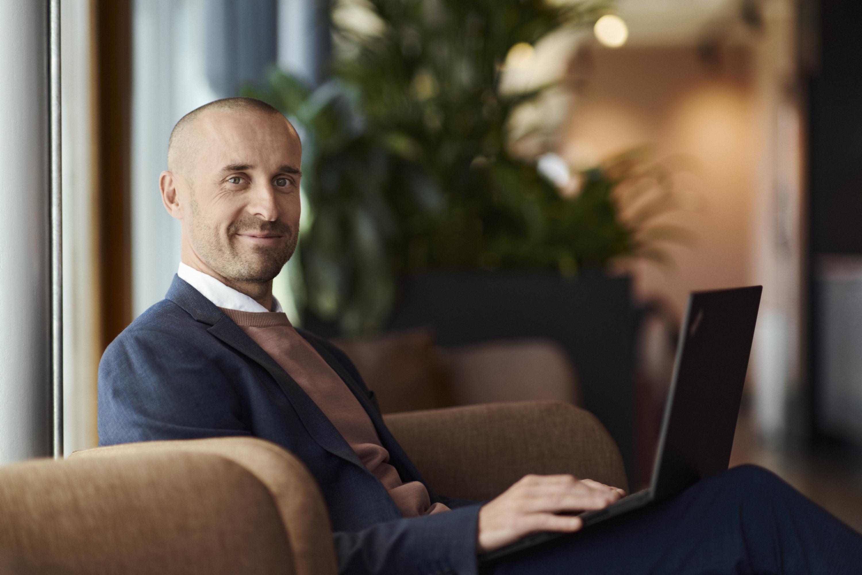 En man sitter i en fotölj med en bärbar dator i knät