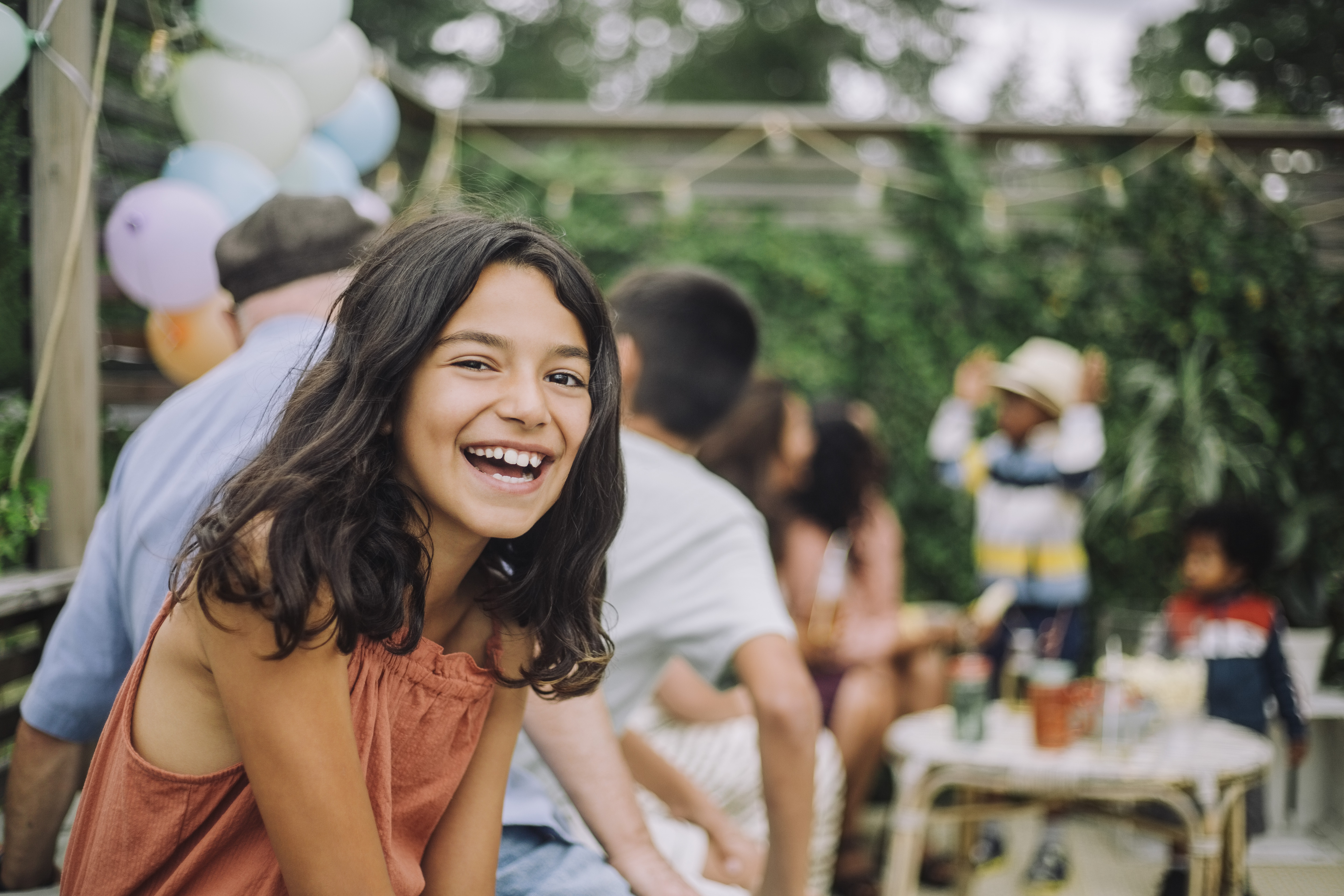 En leende flicka sitter på ett födelsedagskalas, ballonger syns i bakgrunden