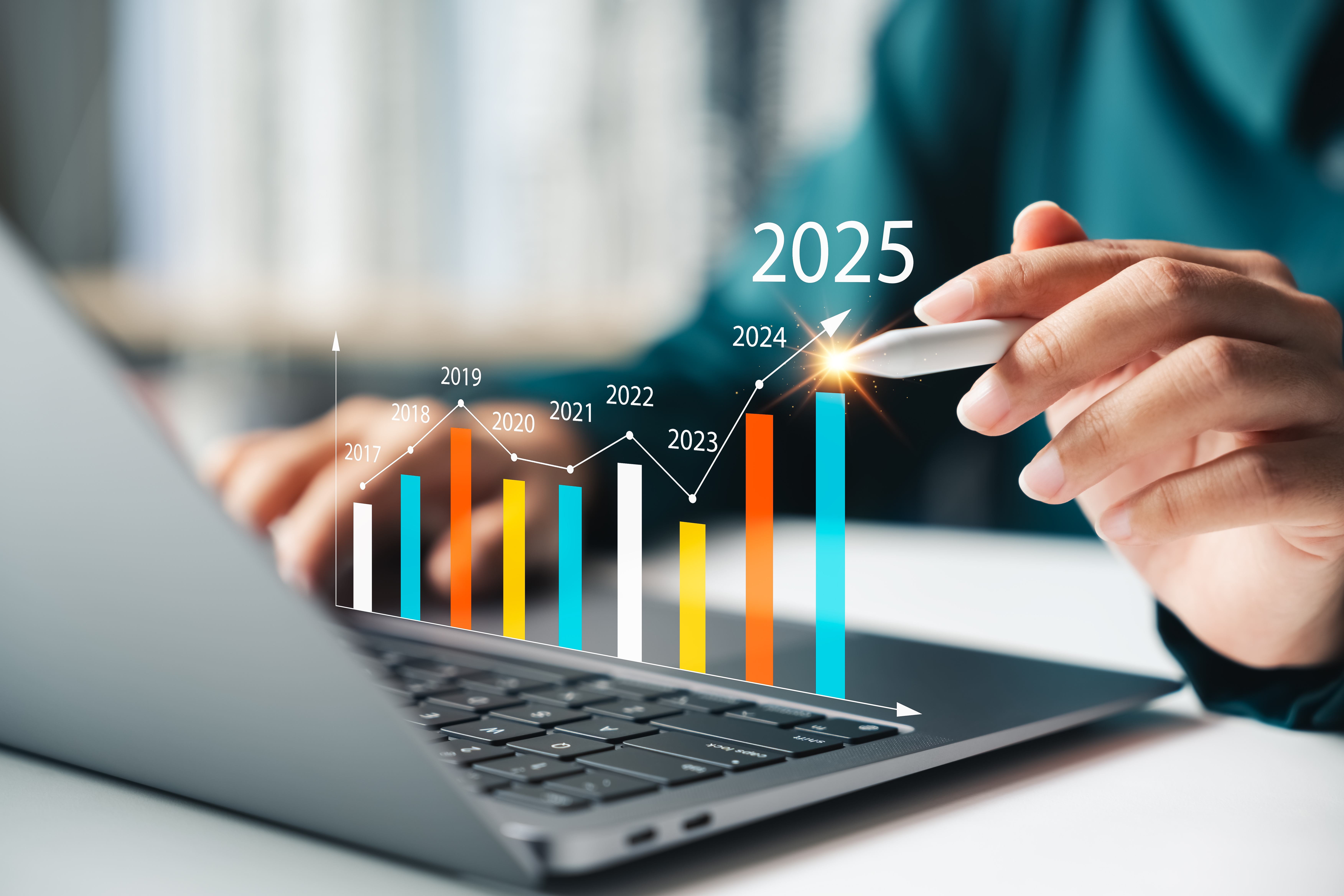 Hand pekar på stigande stapeldiagram framför en bärbar dator med årtalen 2017–2025